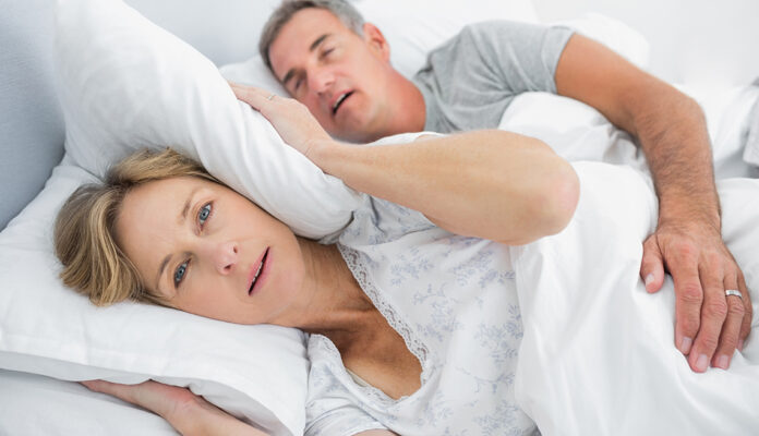 Irritated wife blocking her ears from noise of husband snoring